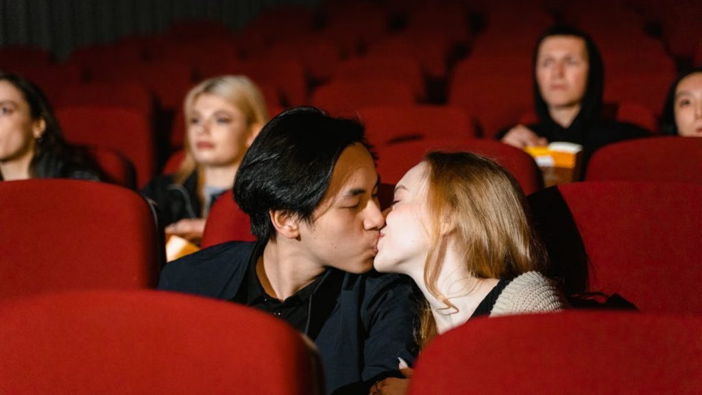 Romantic couple kissing in a cozy movie theater setting.